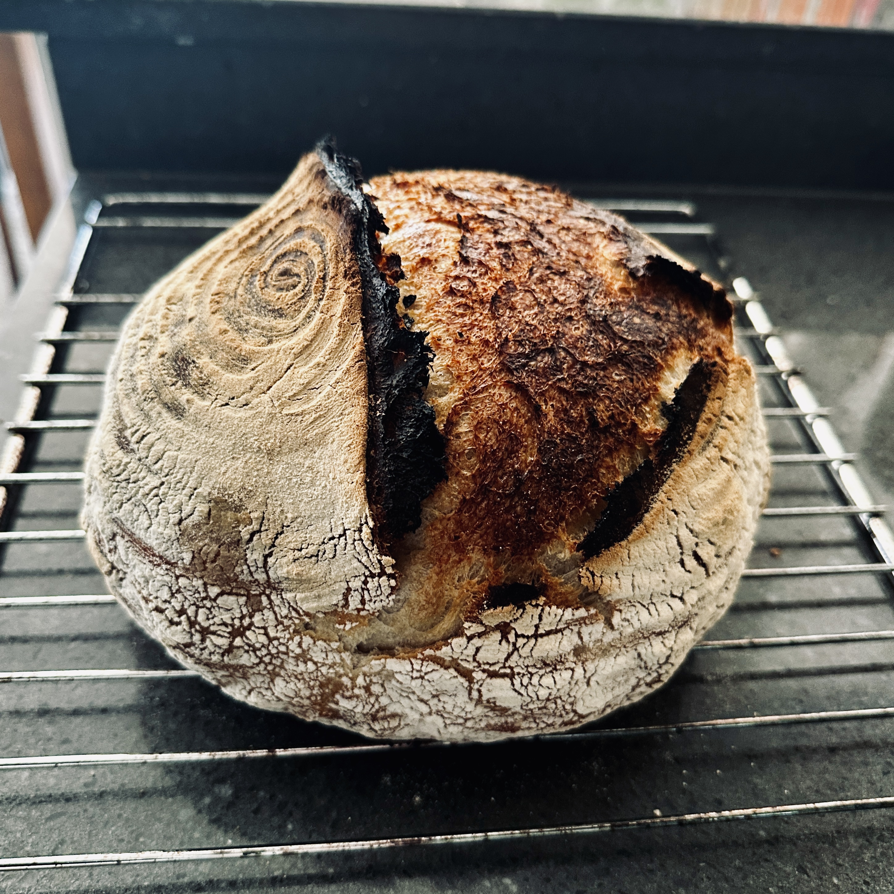 Round sourdough boule with a dark blistered crust cooling on a wire rack.